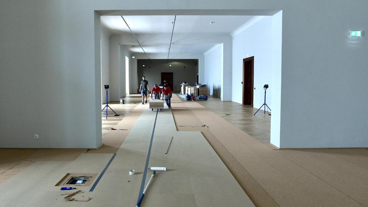 Eine Malerrolle liegt auf dem mit Pappe abgedeckten Parkett eines Museumssaal. Arbeioter schieben im Sommer 2018 Spanplatten durch den großen Raum, in dem später Ausstellungen des "Hauses der Geschichte" in Wien stattfinden sollen.