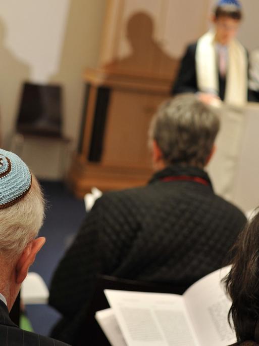 Bar-Mitzwa-Gottesdienst in der liberalen jüdischen Gemeinde Beth Shalom in München. Zu sehen sind Gemeindemitglieder mit Kippa, weiter hinten der Rabbiner mit einem Jungen, der auf die Bar Mitzwa vorbereitet wird.