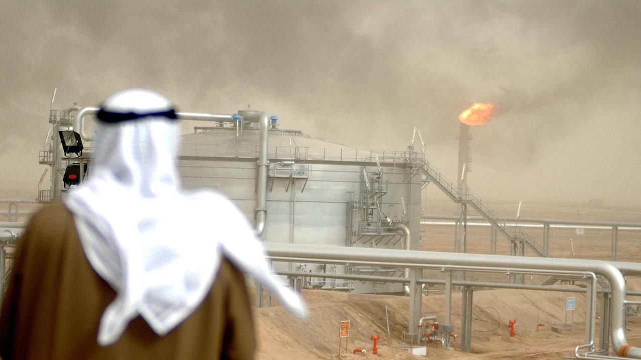 Ein Mann mit weißer Kufiya schaut auf ein Ölfeld mit einer Industrieanlage. Ein Mann mit weißer Kufiya schaut auf ein Ölfeld mit einer Industrieanlage.
