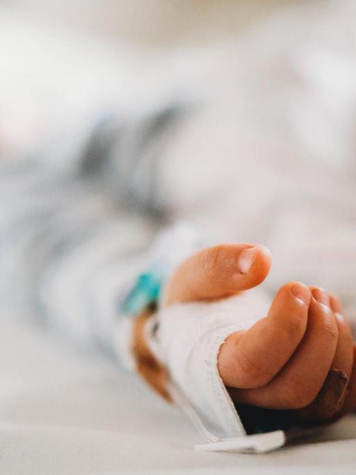 Aufnahme eines Kindes im Krankenhausbett, die Schärfe liegt auf der Hand des Kindes.
