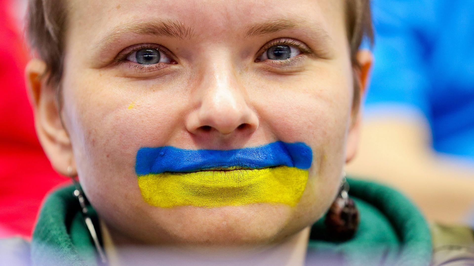 Eine Frau hat ihren Mund mit den Farben ukrainischen Flagge ummalt.