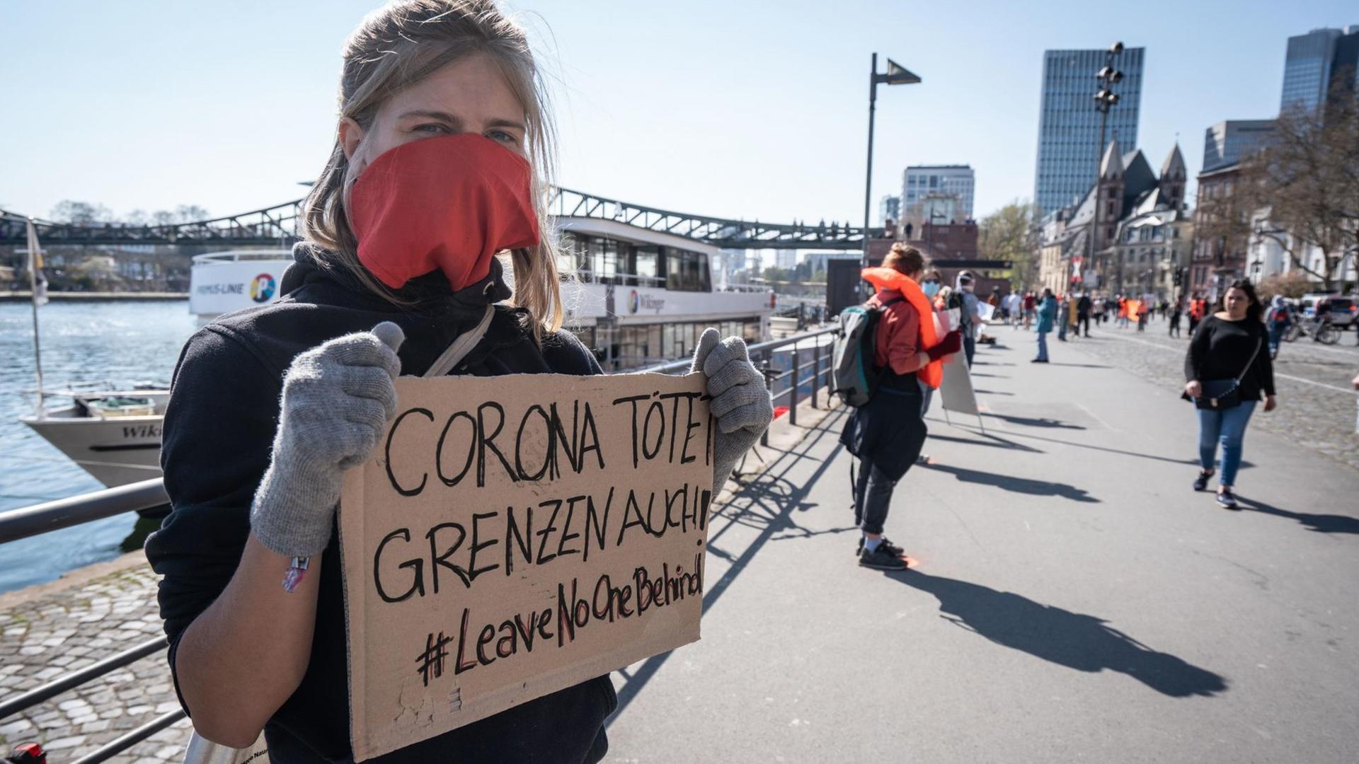 Mehrere Menschen stehen mit Mindestabstand und Schildern für #leavenoonebehind in Frankfurt am Main.