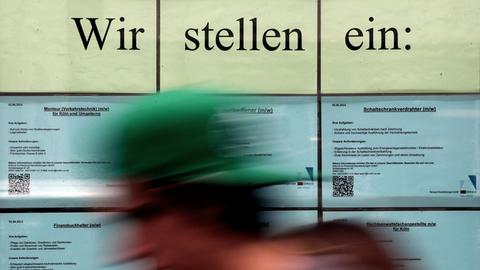 Stellenanzeigen hängenim Fenster einer Zeitarbeitsfirma. Davor ist schemenhaft eine Person zu erkennen.