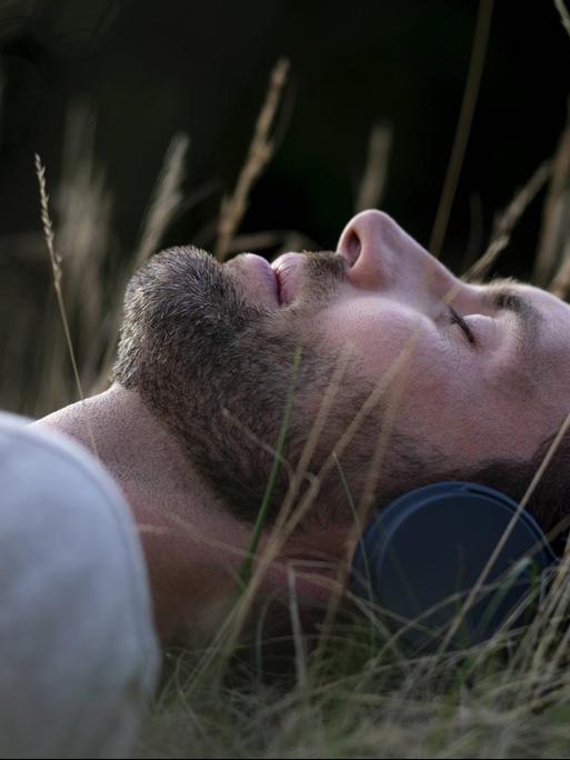 Ein junger Mann liegt schlafend auf einer Wiese und hört Musik.