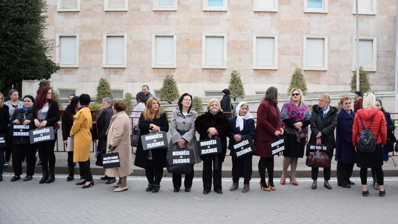 Eine Gruppe von Frauen vor einem Wohnblock. Die Frauen halten Schilder in den Händen, auf denen steht: "Gelegenheit, Gleichheit, Wahlmöglichkeit" und "Sexuelle Gleichheit, ökonomische Gerechtigkeit".