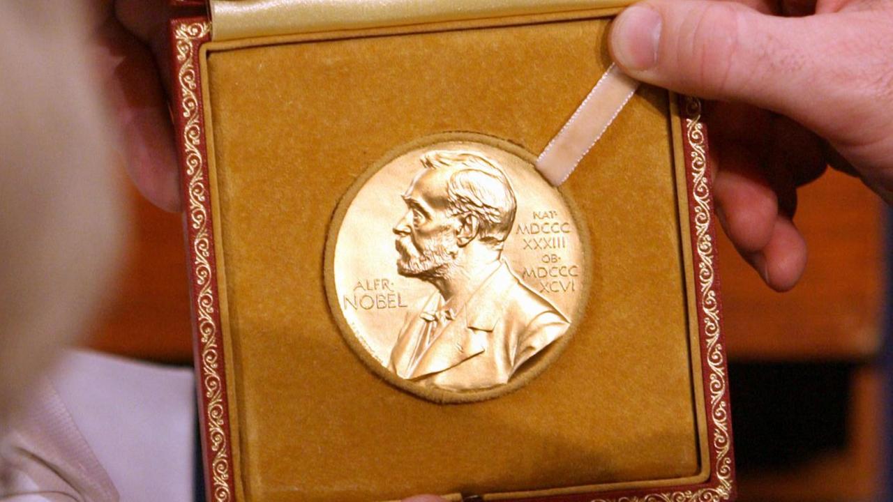 Mehrere Hände halten die Medaille mit dem Konterfei von Alfred Nobel
