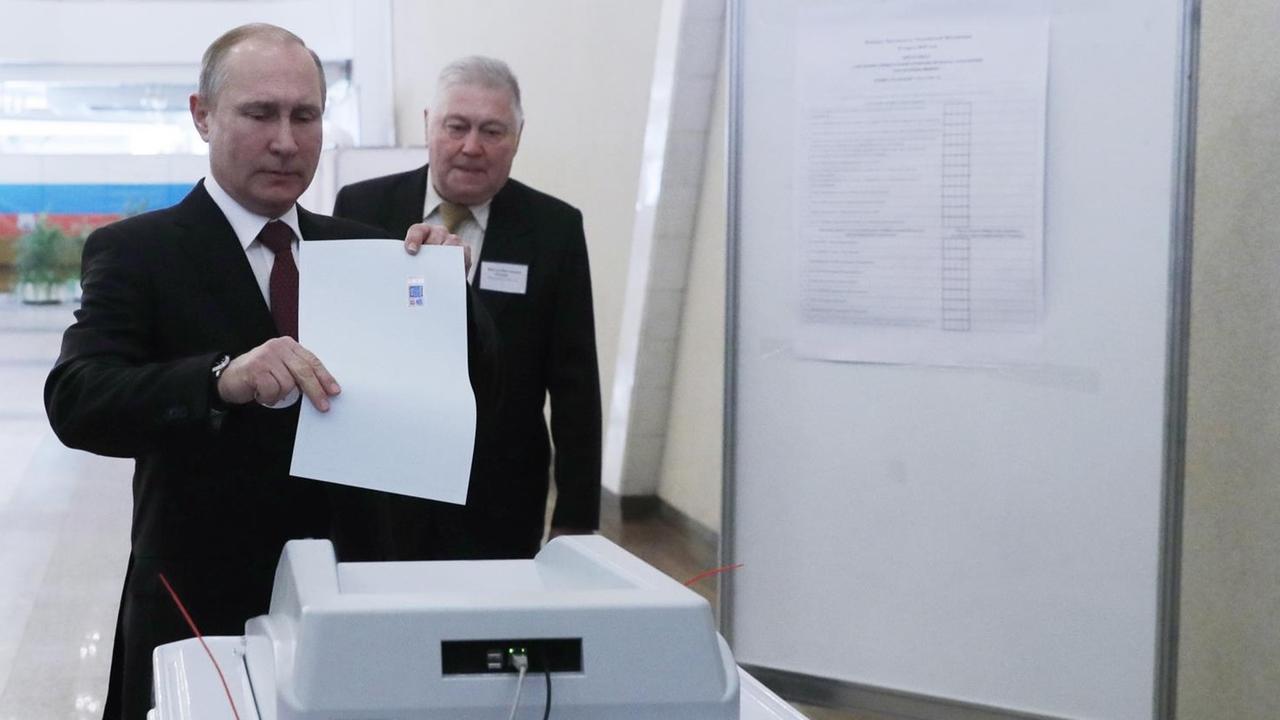 Der russische präsident Putin wirft seinen Wahlzettel in eine Urne.