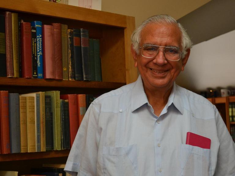 Der Theologe Justo González, ein ergrauter Mann, freundlich lächelnd vor einem Bücherregal in seiner Wohnung