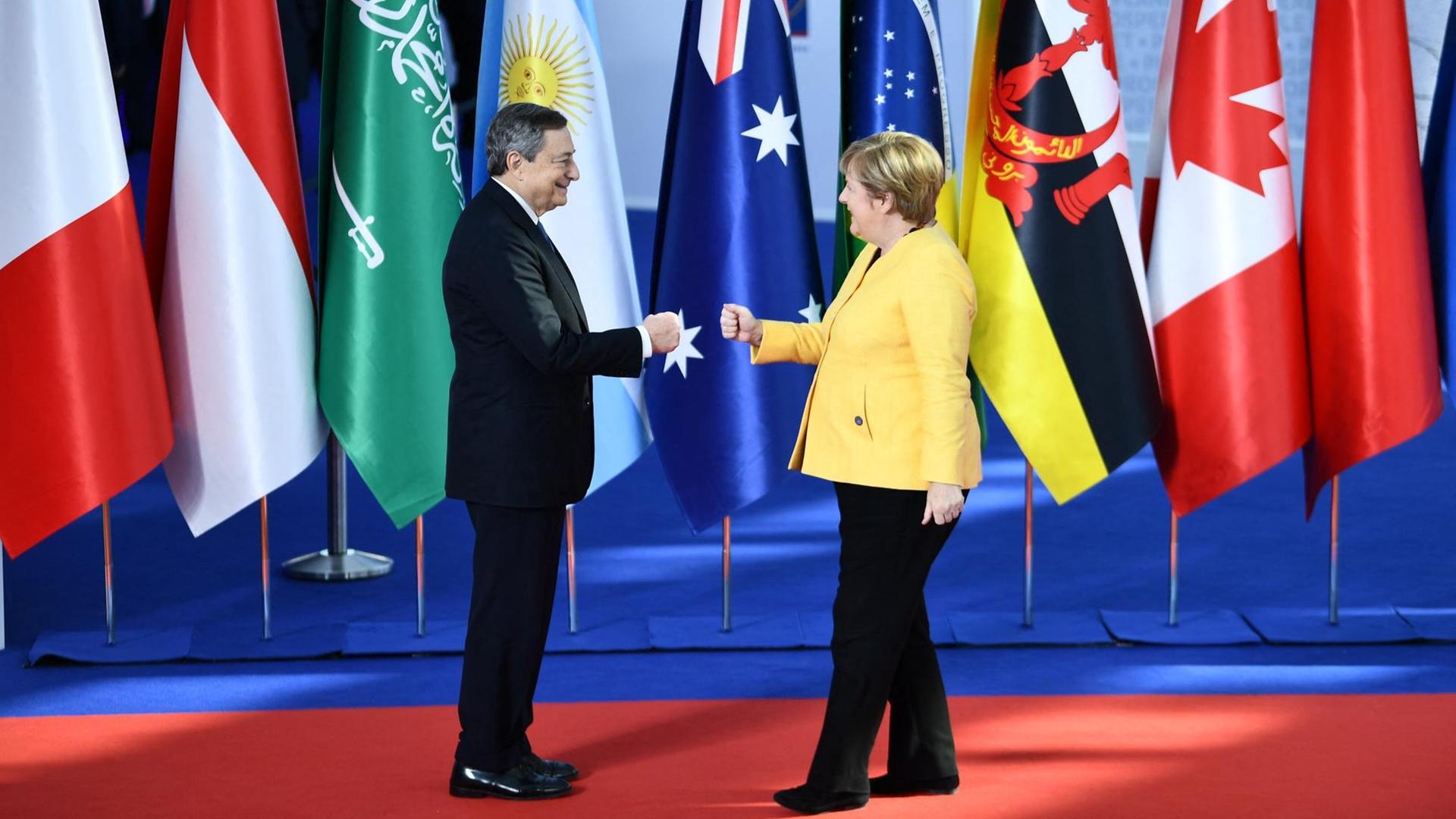 Draghi und Merkel geben sich die Hand. Hinter ihnen stehen die Fahnen von den G-20-Ländern.