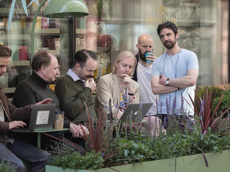 Menschen haben sich auf der Straße zu einer Gruppe zusammengefunden und schauen auf ein Laptop.