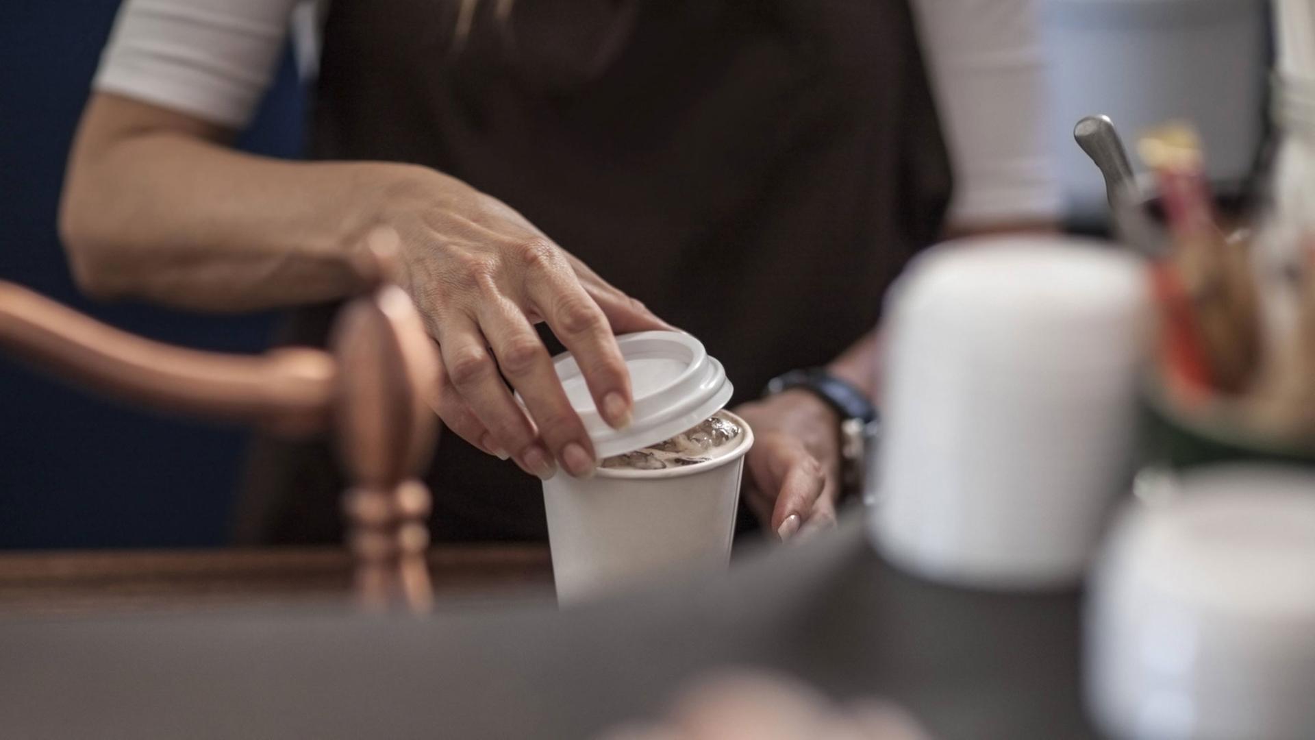 Ein Barista legt den Deckel auf einen Einweg-Kaffeebecher voller Kaffee.