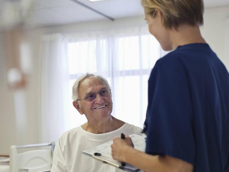 Eine Krankenpflegerin im Gespräch mit einem älteren Patienten