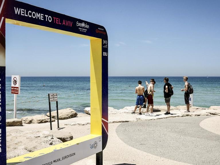 Touristen stehen mit Blick auf das Mittelmeer neben einem Werbeschild für den Eurovision Song Contest 2019. Vom 14. bis 18. Mai 2019 veranstaltet die Küstenstadt den internationalen Gesangswettbewerb Eurovision Song Contest (ESC)