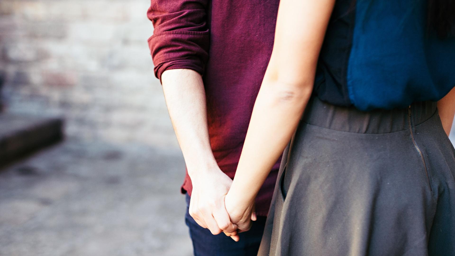 Zwei Personen stehen nahe beieinander und halten sich an der Hand.