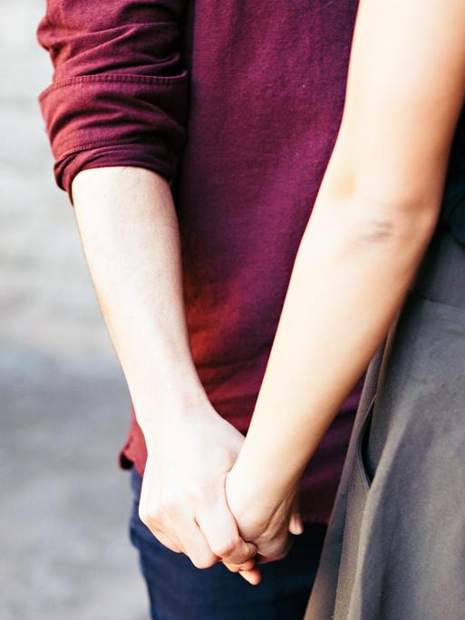 Zwei Personen stehen nahe beieinander und halten sich an der Hand.
