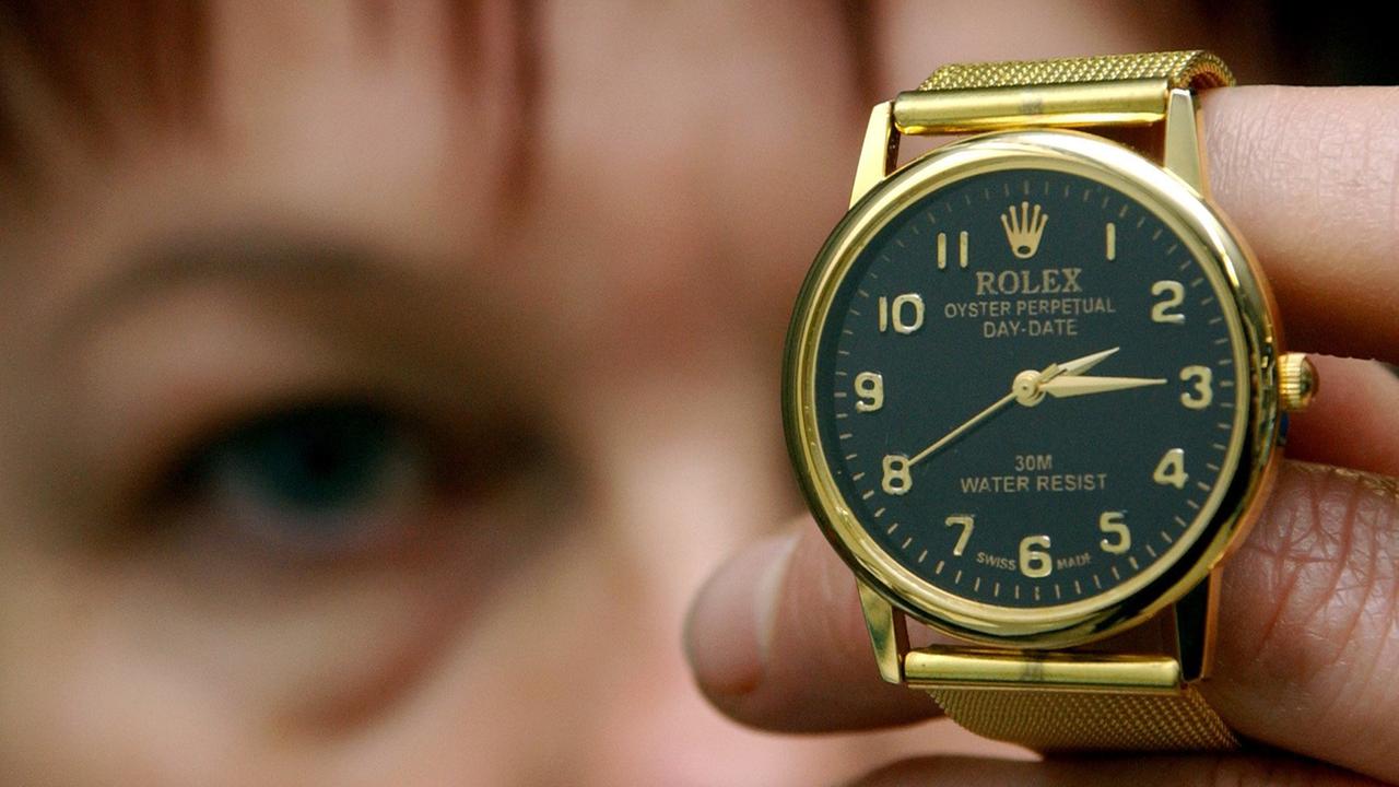 Eine Frau hält eine gefälschte Rolex-Uhr in die Kamera.