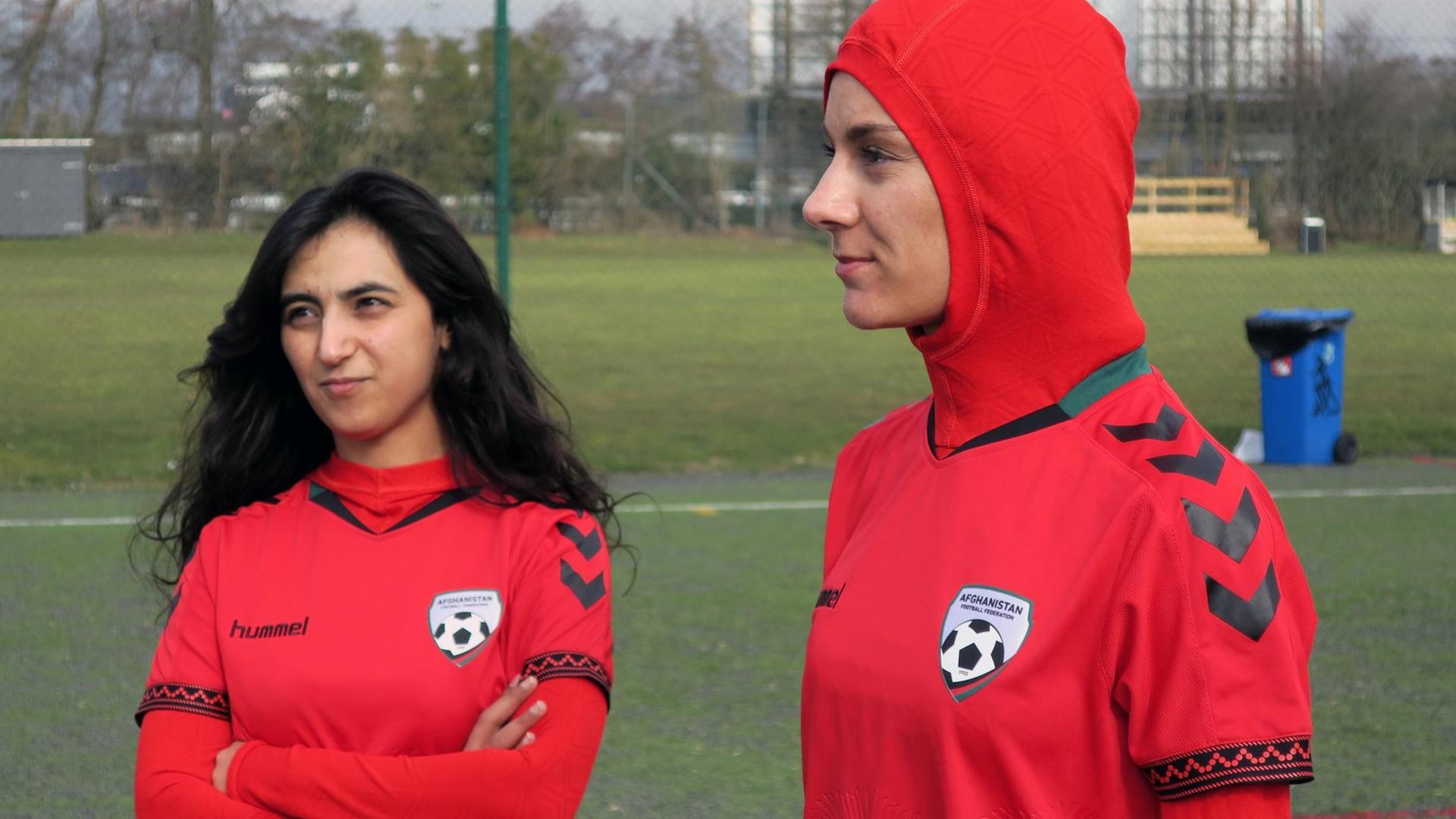 Shabnam Mabarz und Khalida Popal (l.), stehen im Trikot der afghanischen Frauen-Nationalmannschaft auf einem Fußballfeld.