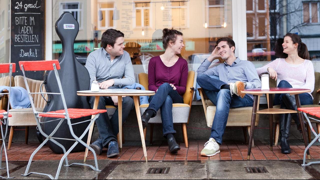 Die Quartettmitglieder sitzen in Jeans in einem Straßenkaffee.