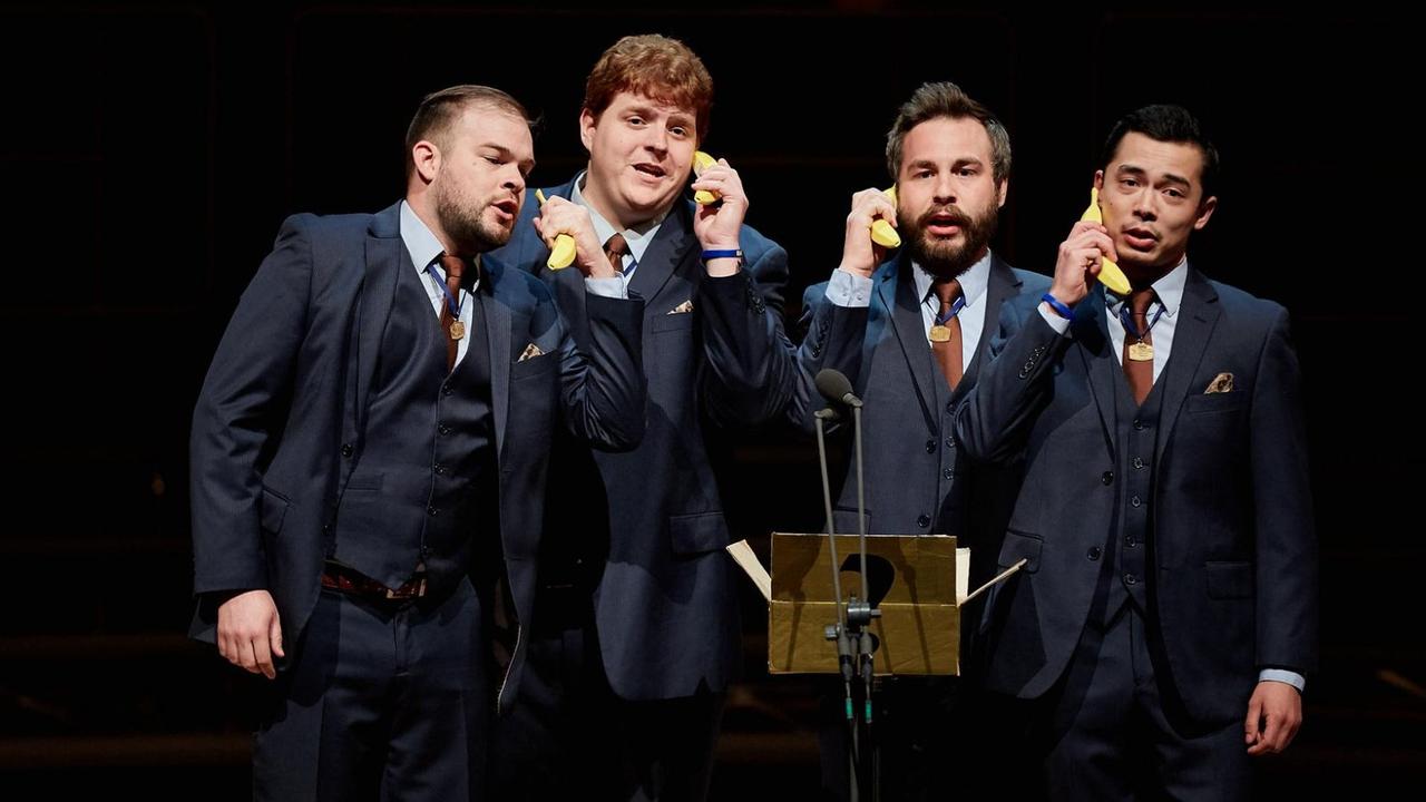 Vier Sänger in Anzügen halten sich jeweils eine Banane ans Ohr, als sei sie ein Handy.