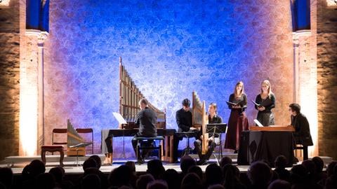 Ensemble Tasto Solo mit historischem Instrumentarium auf der Bühne einer Kirche vor blau angestrahltem Hintergrund