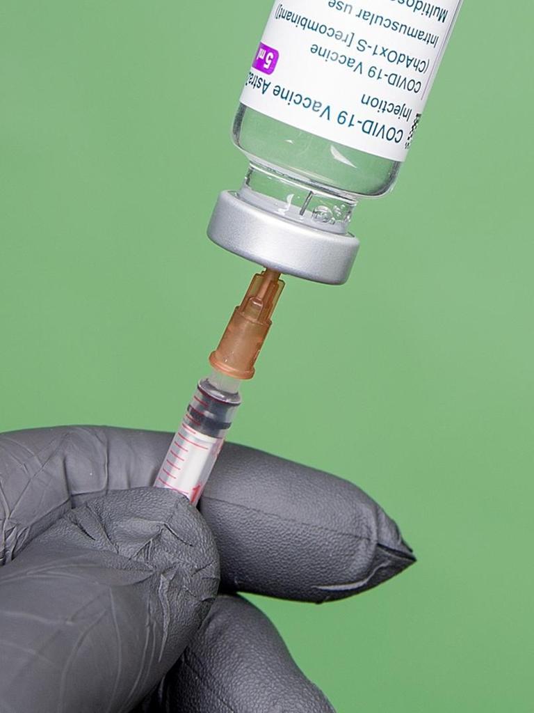  Eine Person mit einem grauen Schutzhandschuh vor grünem Hintergrund, zieht mit Hilfe einer Impfspritze eine Impfdosis auf