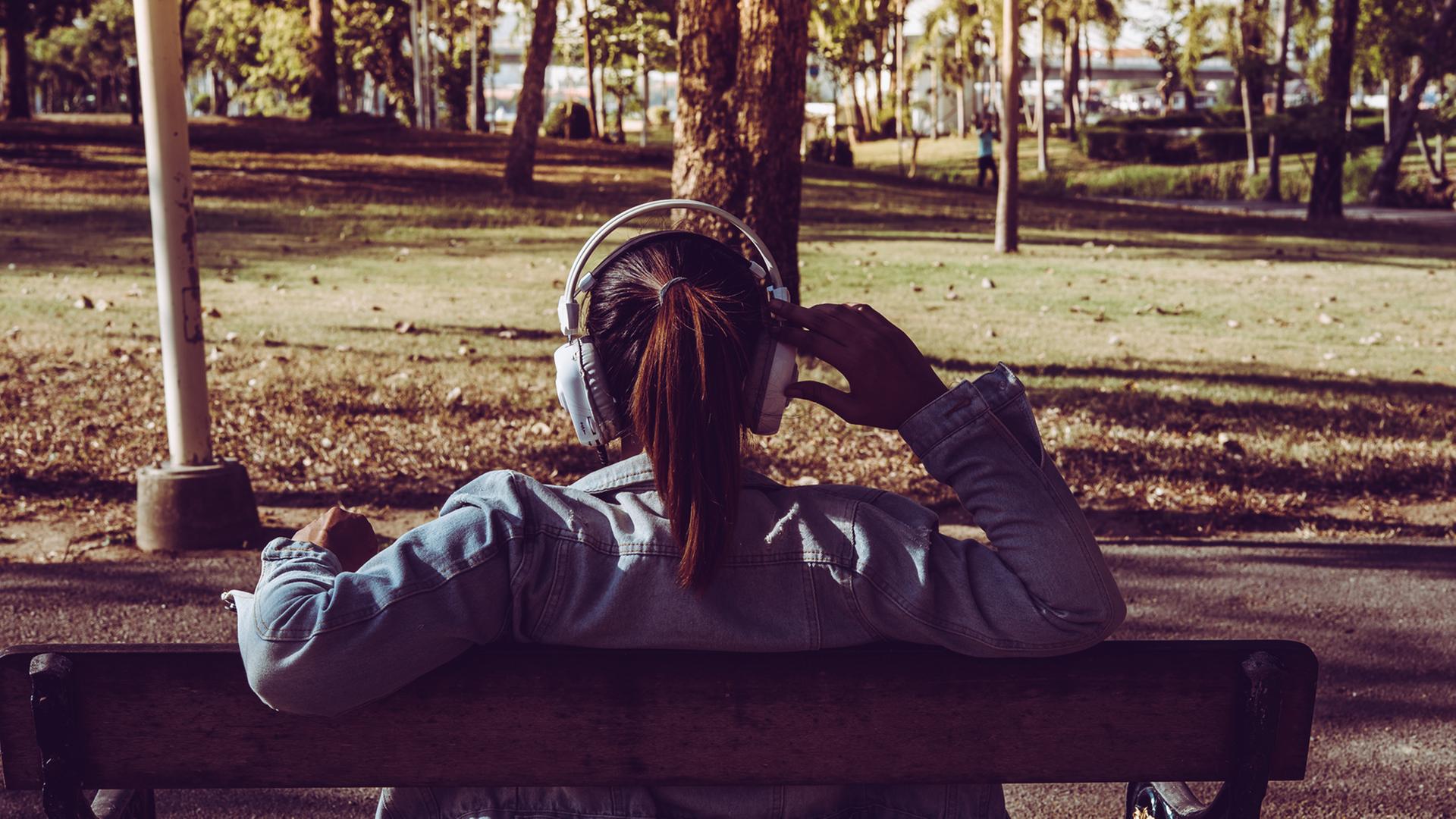 Die Parkbank ist eine Station der akustischen Reise. Eine junge Frau sitzt mit Kopfhörern auf einer Parkbank. 