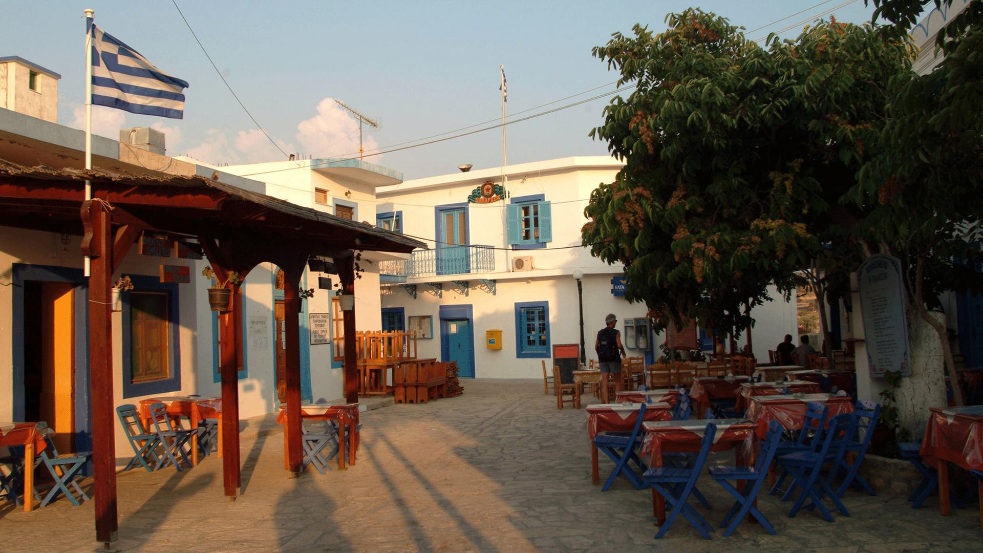 Dorfplatz von Ormos Sokoro mit griechischer Fahne und einem leeren Straßencafe.