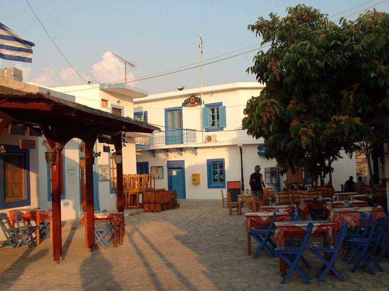 Dorfplatz von Ormos Sokoro mit griechischer Fahne und einem leeren Straßencafe.