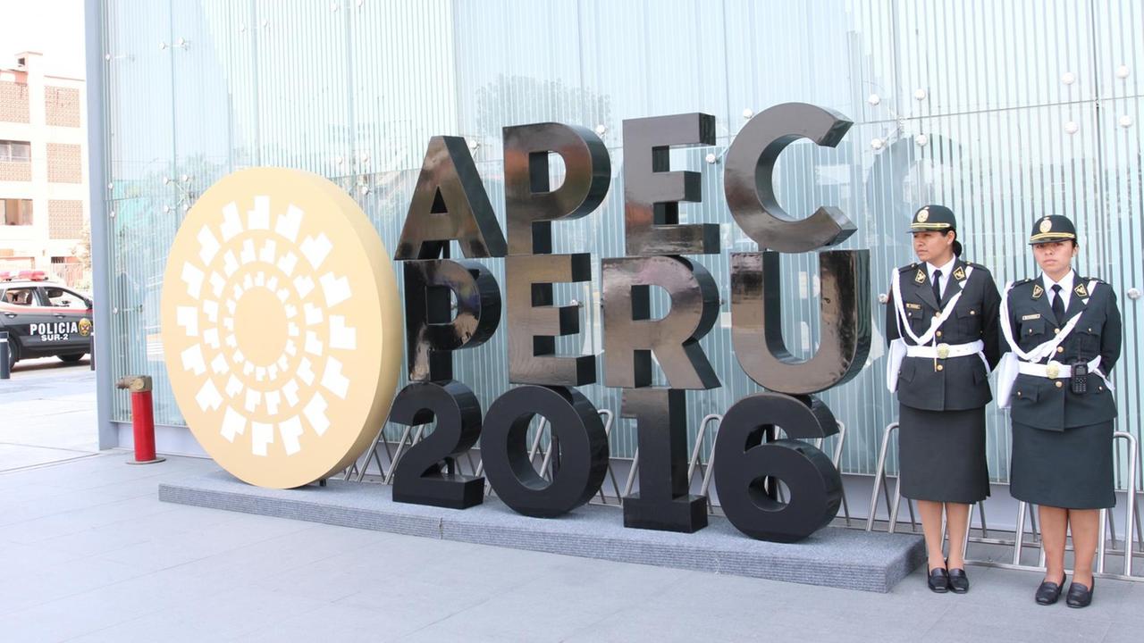 Zwei uniformierte Frauen stehen in Lima neben demSchriftzug "Apec Peru 2016"