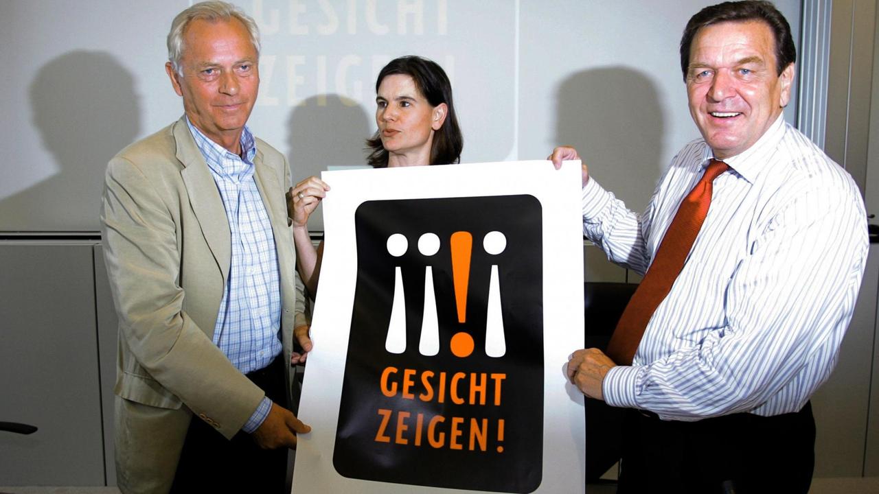 Gerhard Schröder, Uwe-Karsten Heye und Sophia Oppermann mit einem Plakat mit der Aufschrift "Gesicht zeigen!"