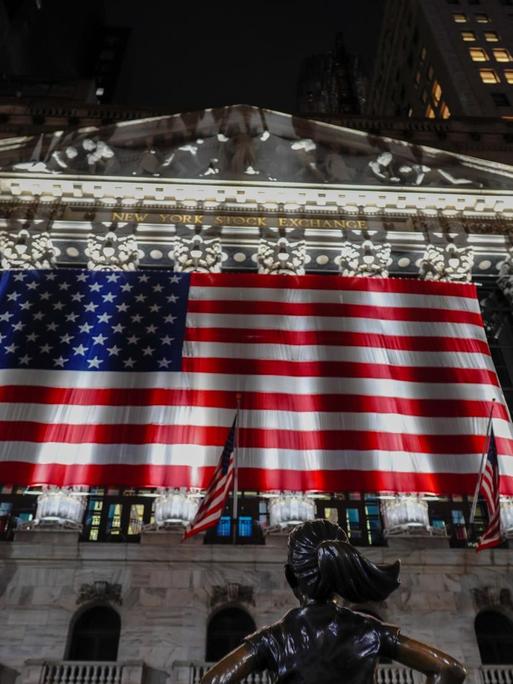 Die Börse an der New Yorker Wall Street ist mit der US-Flagge geschmückt, die von Scheinwerfern angeleuchtet werden.