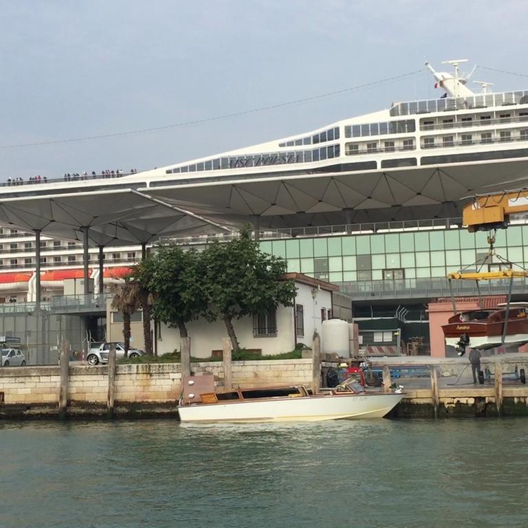 Ein riesiges Kreuzfahrtschiff überragt venezianische Hafenanlagen
