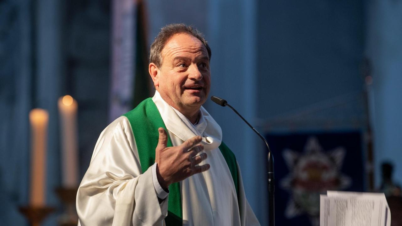 Rainer Maria Schießler, Pfarrer in München, spricht in einer Kirche. Hinter ihm sind Kerzen zu sehen. 