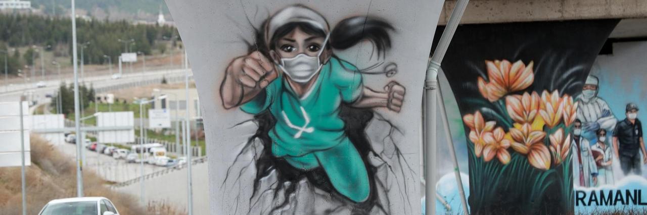 Auf einem Brückenpfeiler ist eine Ärztin in Schutzkleidung dargestellt, die in der Pose einer Superheldin eine Mauer durchbricht