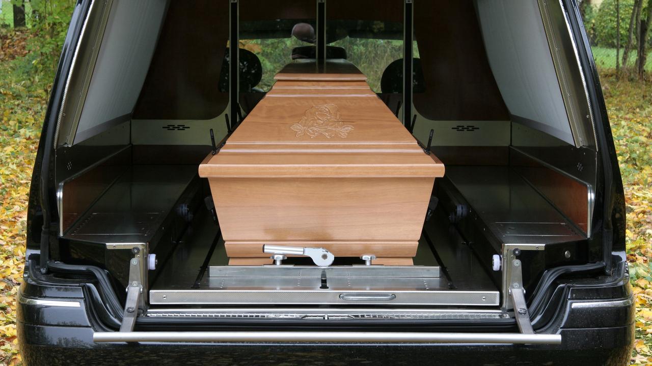 Ein Holzsarg in einem Auto eines Bestattungsunternehmens bei einer Beerdigung