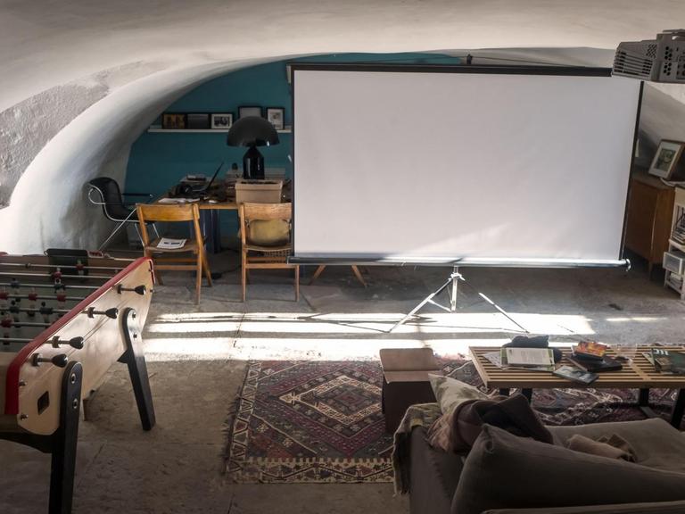 Ein Sofa, davor eine Leinwand und ein Videoprojektor.