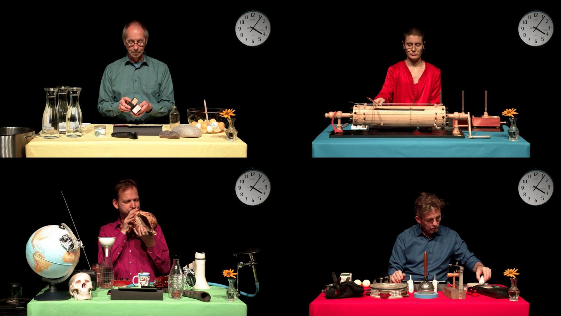 Ausschnitt einer Videoperformance: Drei Männer und eine Frau sitzen an vier verschieden arrangierten Einzeltischen. Jeder hat Instrumente und Alltagsgegenstände darauf. Im Hintergrund hängt je eine Uhr, die 4:06 Uhr zeigt.