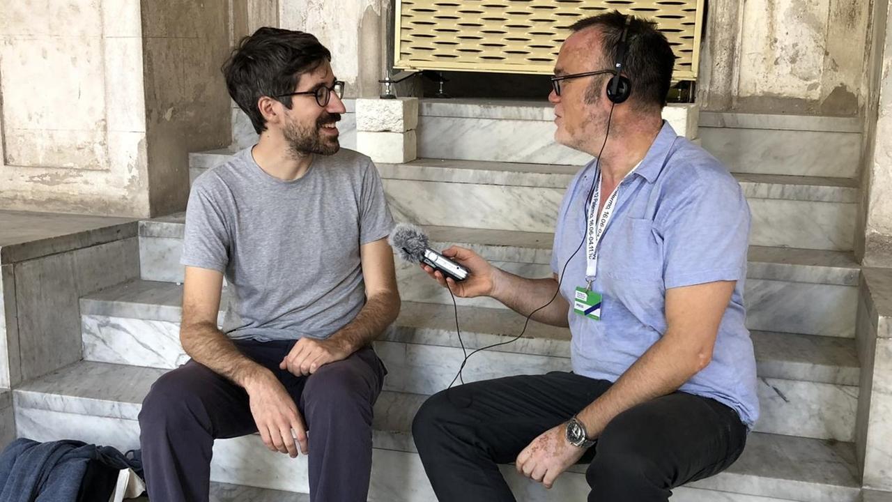 Lorenzo Pezzani auf einer Mamorsteintreppe sitzend in Italien im Interview mit Moderator Vladimir Balzer