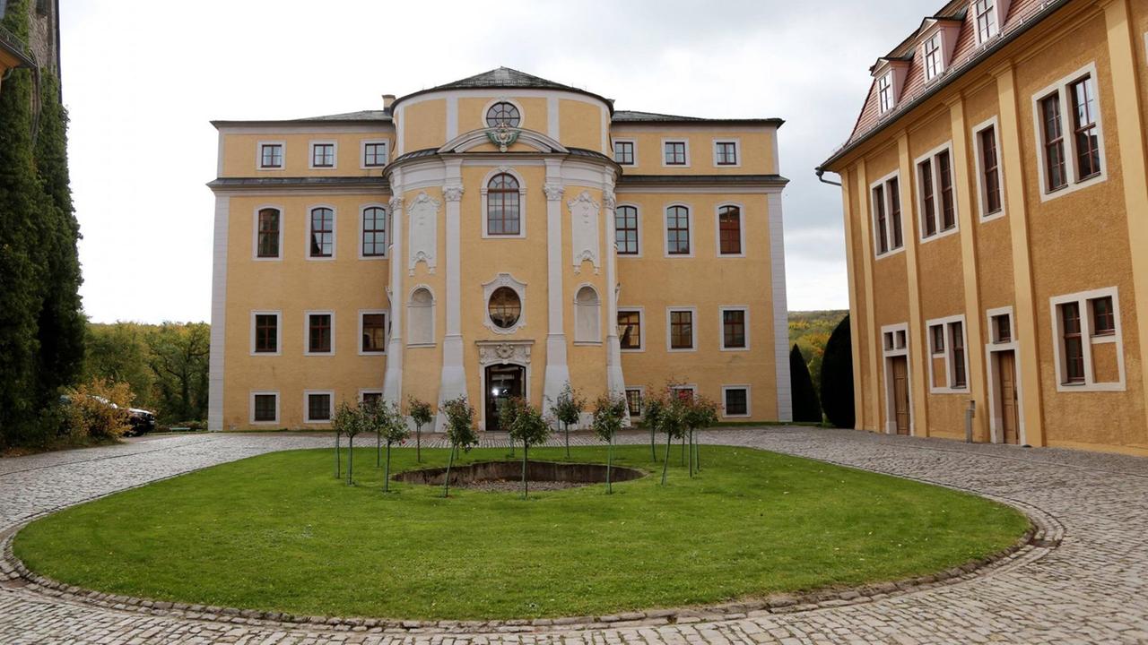 Blick auf eine runde Auffahrt direkt vor einem gelben, kleinen Schlossbau.