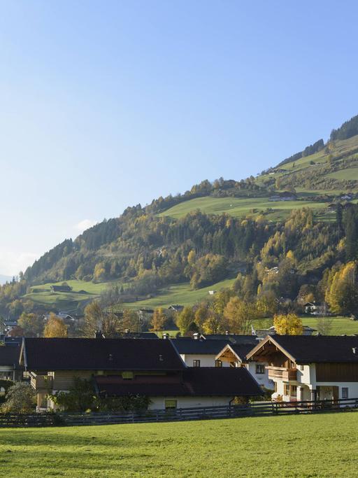 Blick auf das Dorf Stuhlfelden im Salzburger Land in Österreich: Hinter dem Dorf sind Berge und darüber blauer Himmel zu sehen.