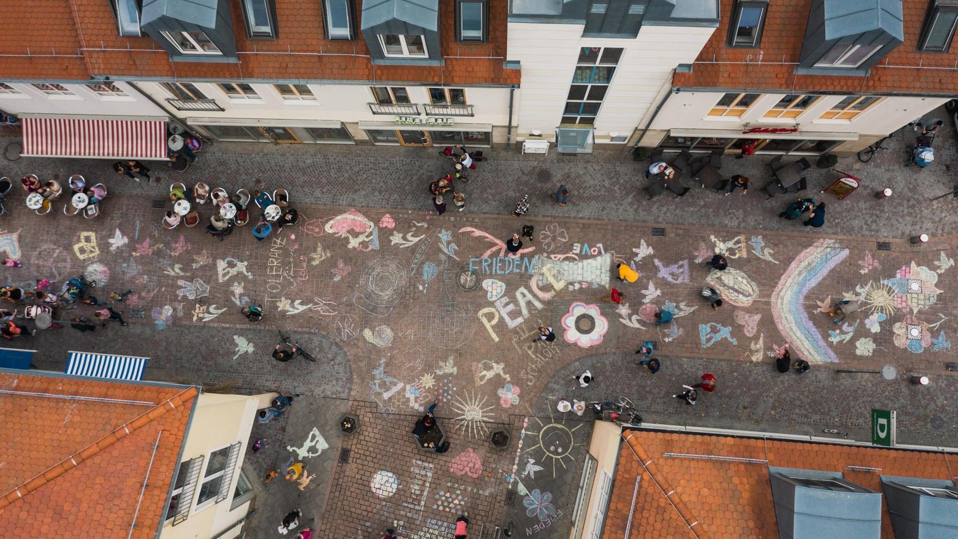 Aus der Luft nach unten fotografiert: Mit Malkreide haben viele Bürgerinnen und Bürger Friedensbotschaften auf den Boden einer Straße in der Nähe des Marktplatzes gemalt und geschrieben.