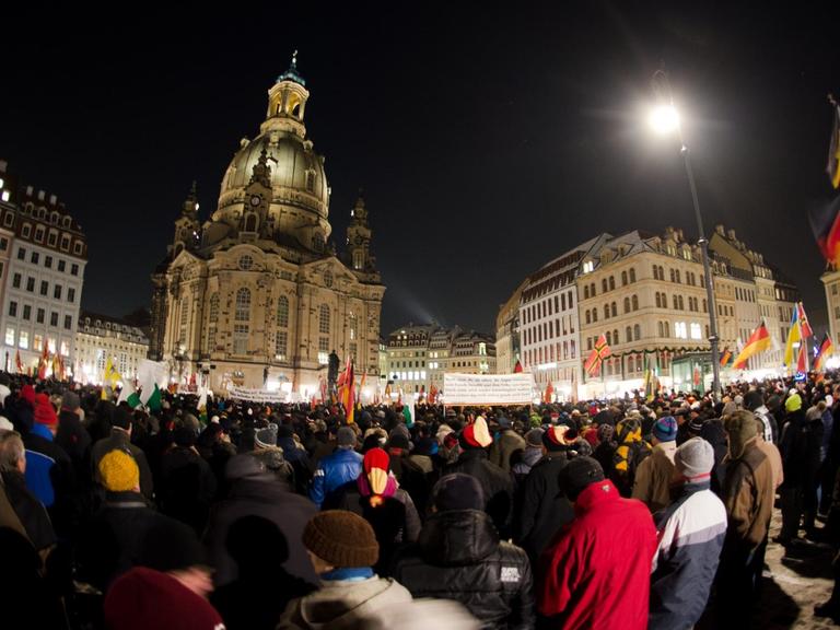 Menschenmenge mit Deutschlandfahnen vor der Dresdner Frauenkirche bei Dunkelheit.