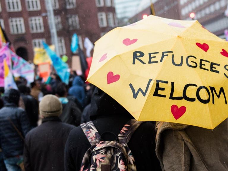 Eine Frau und ein Mann mit einem Regenschirm mit der Aufschrift "Refugees welcome" nehmen in der Innenstadt in Hamburg an einer Demonstration für die Rechte von Flüchtlingen teil.