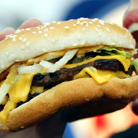 Ein Mund ist weit geöffnet, um in einen Cheeseburger zu beißen.