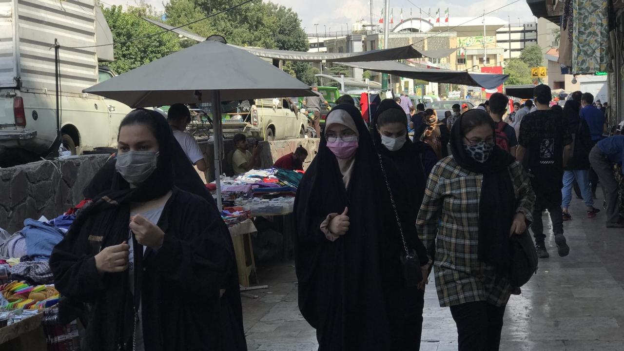 Eine belebte Einkaufststraße und Frauen mit unterschiedlichen Kopfbedeckungen.