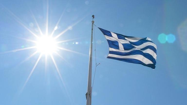 Die griechische Flagge ist hier auf der Akropolis zu sehen, darunter stehen Menschen