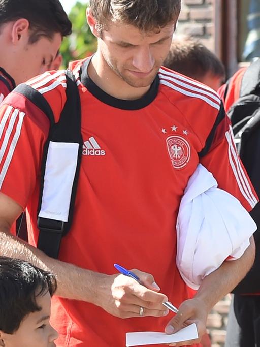 Fußballer Thomas Müller gibt einen kleinen Jungen im Brasilien-Trikot ein Autogramm am Rande der Weltmeisterschaft 2014.