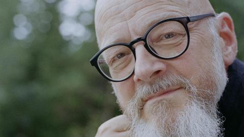 Ein Mann mit eckiger schwarzer Brille und langem weißen Bart blickt freundlich in die Kamera. Es ist der Organist Hans-Ola Ericsson.