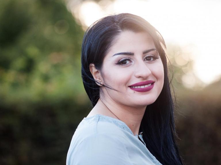 Ein Porträtfoto von Rana Ahmad, eine junge Frau mit langem schwarzem Haar blickt lächelnd über ihre Schulter in die Kamera
