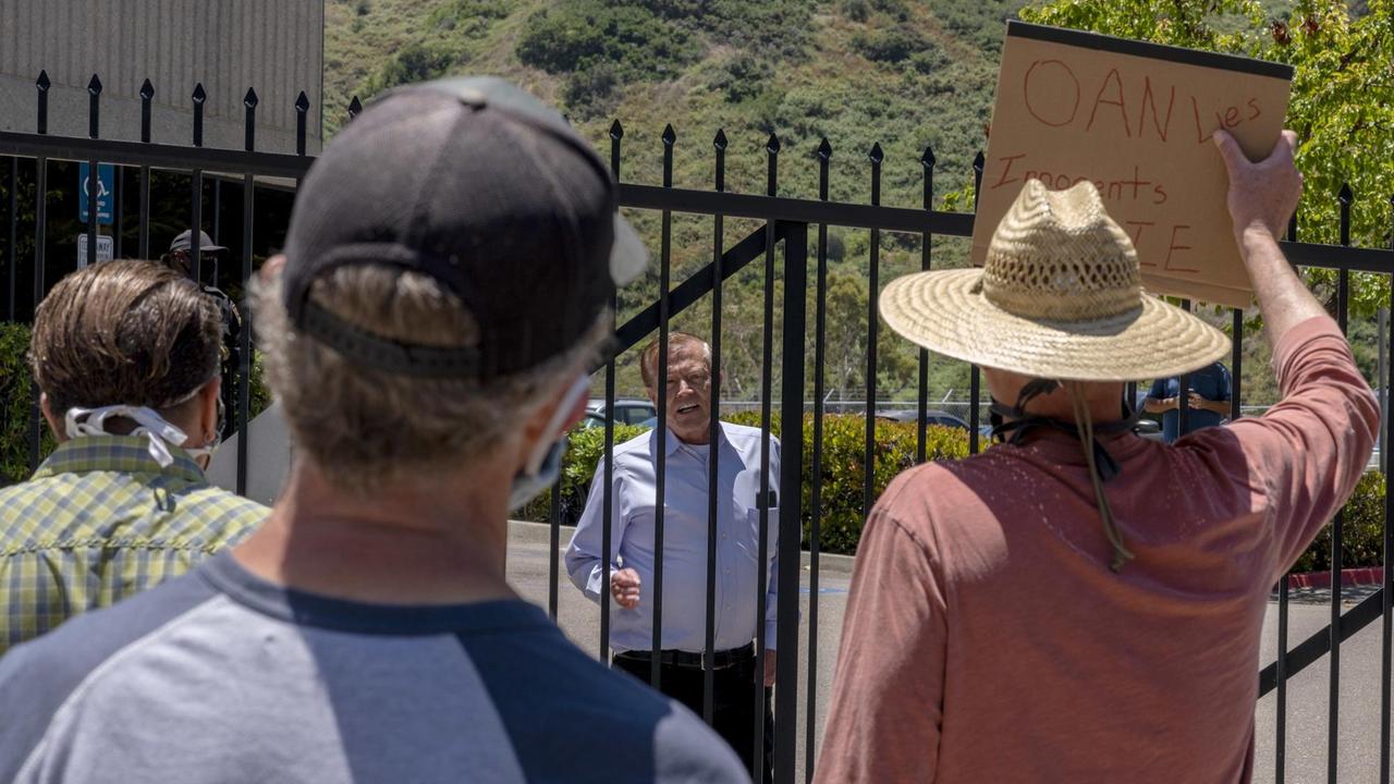 Der Gründer des Senders OAN, Robert Herring Senior, spricht durch einen Zaun mit Protestierenden.